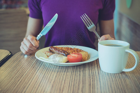 位轻女子坐咖啡馆的张桌子旁,准备享用顿传统的英式早餐图片