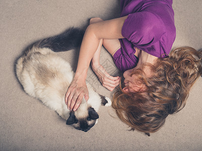 位轻女子躺家里的地毯上,抚摸着只猫图片