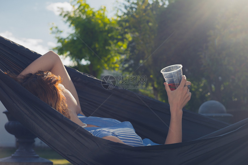 个轻的女人手里着杯饮料,阳光明媚的夏天,她正花园里的吊床上放松图片