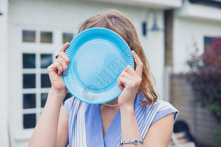 个轻的女人把脸藏花园里的个蓝色纸盘后图片