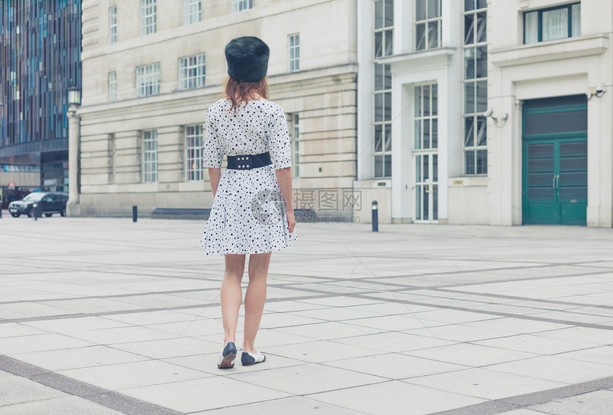 个轻的女人戴着顶毛皮帽子件带黑点的白色连衣裙,走个广场上图片