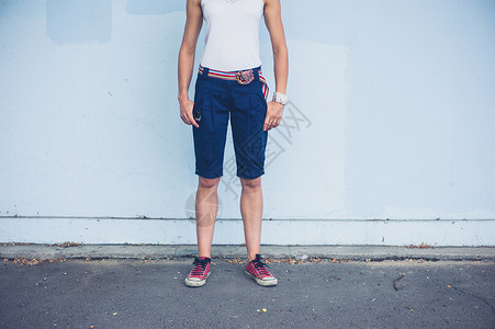 个穿着短裤的时髦轻女人站外的蓝色墙边图片
