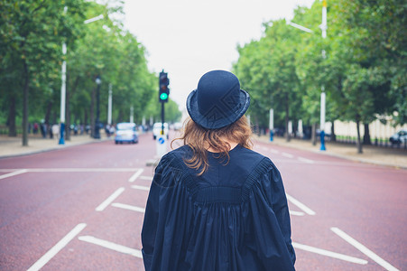 个轻的女人戴着礼帽毕业礼服,走条宽阔的大道上图片