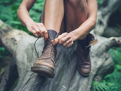 个轻的女人坐森林里的根木头上,正系靴子图片