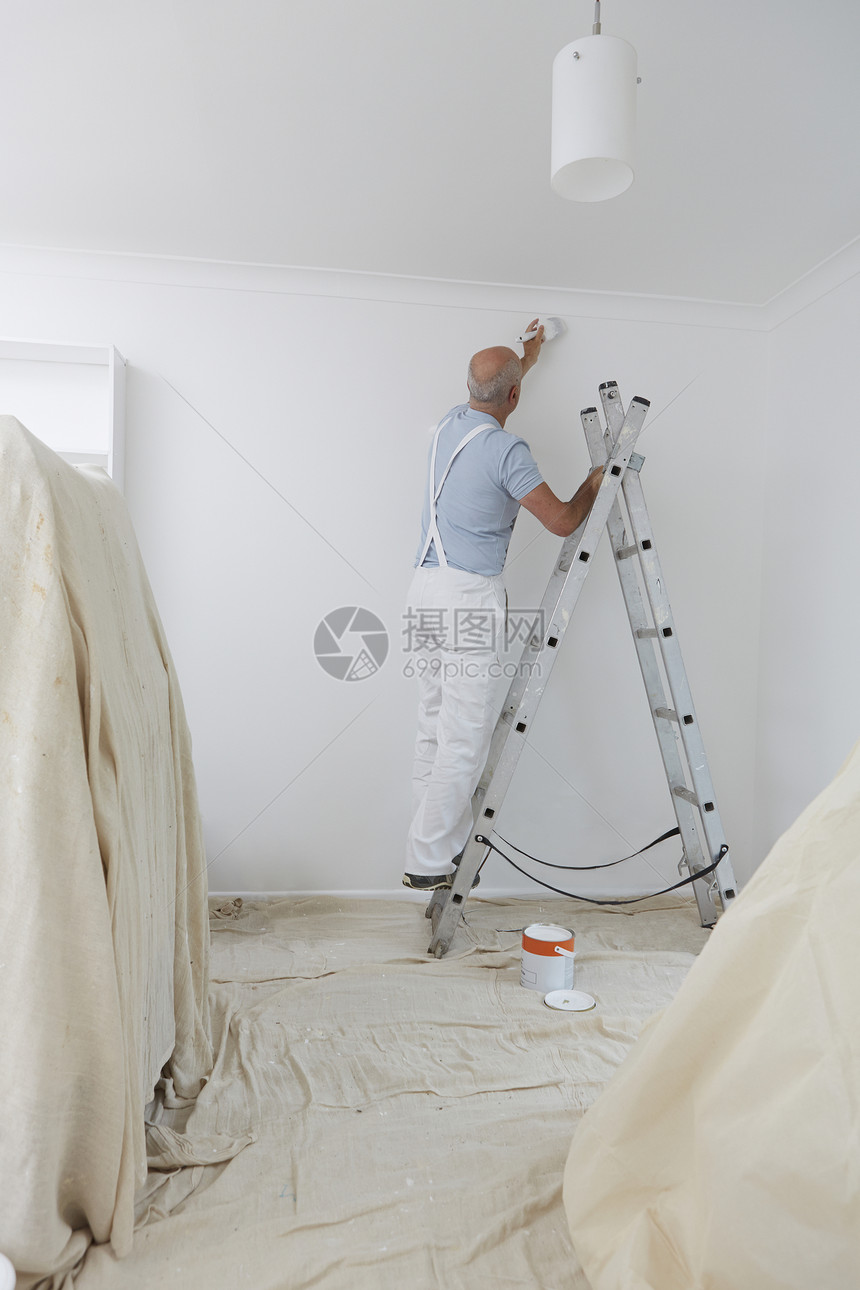 男人梯子上用油漆刷装饰家庭房间图片
