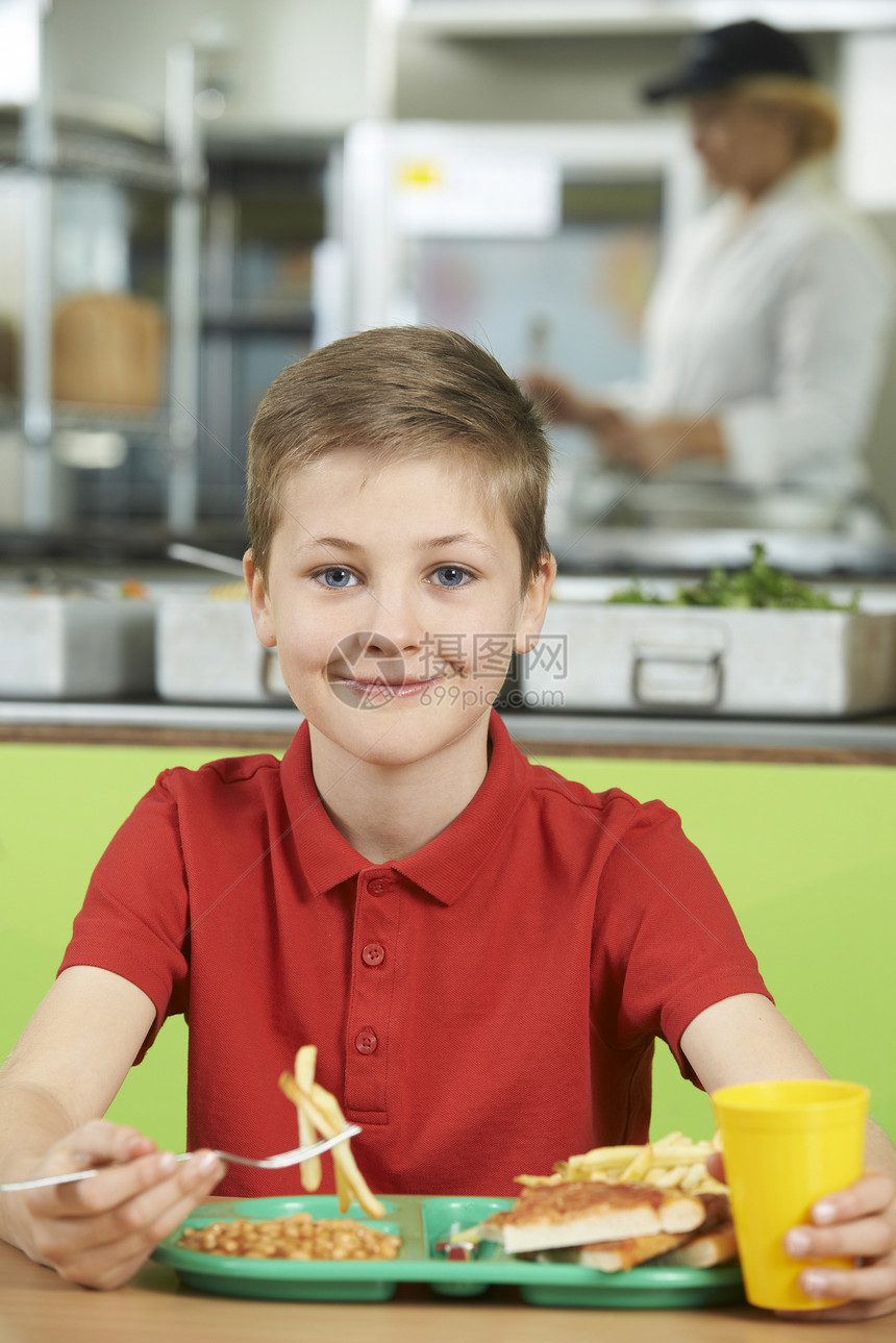 男生坐学校自助餐厅的桌子上吃健康的午餐图片
