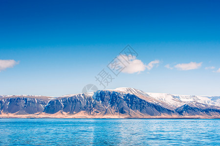 冰岛蔚蓝的大海旁,座山的天空下着雪图片