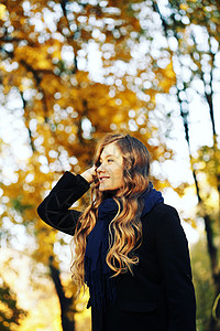 秋天公园里的轻金发女人笑着穿着黑色外套蓝色围巾图片