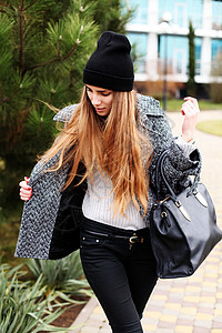 轻时尚感的女人戴着黑色的帽子,温暖的灰色外套皮包摆户外图片