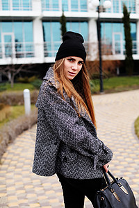 轻时尚感的女人戴着黑色的帽子,温暖的灰色外套皮包摆户外背景图片