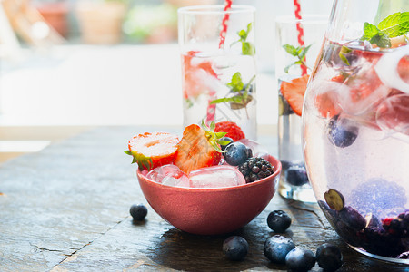 冰块浆果放红碗里,桌子上放着杯水夏季饮料准备图片