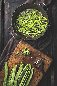 绿色法豆烹饪切片绿色法国豆烹饪锅蔬菜剥皮机黑暗的乡村木制背景,顶部视图图片