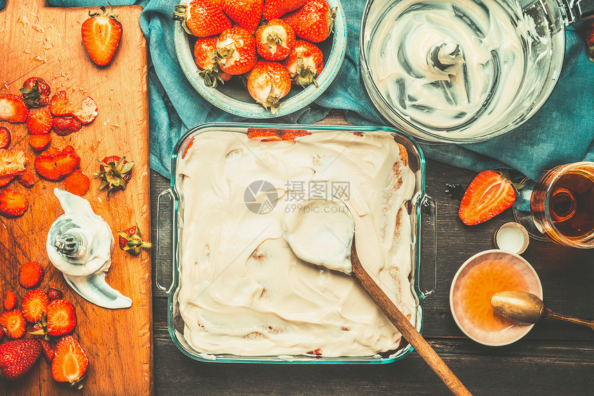 草莓提拉米苏蛋糕制作与蛋糕盘,木制勺子马斯卡彭奶油黑暗的乡村背景,顶部的视野意大利食品图片
