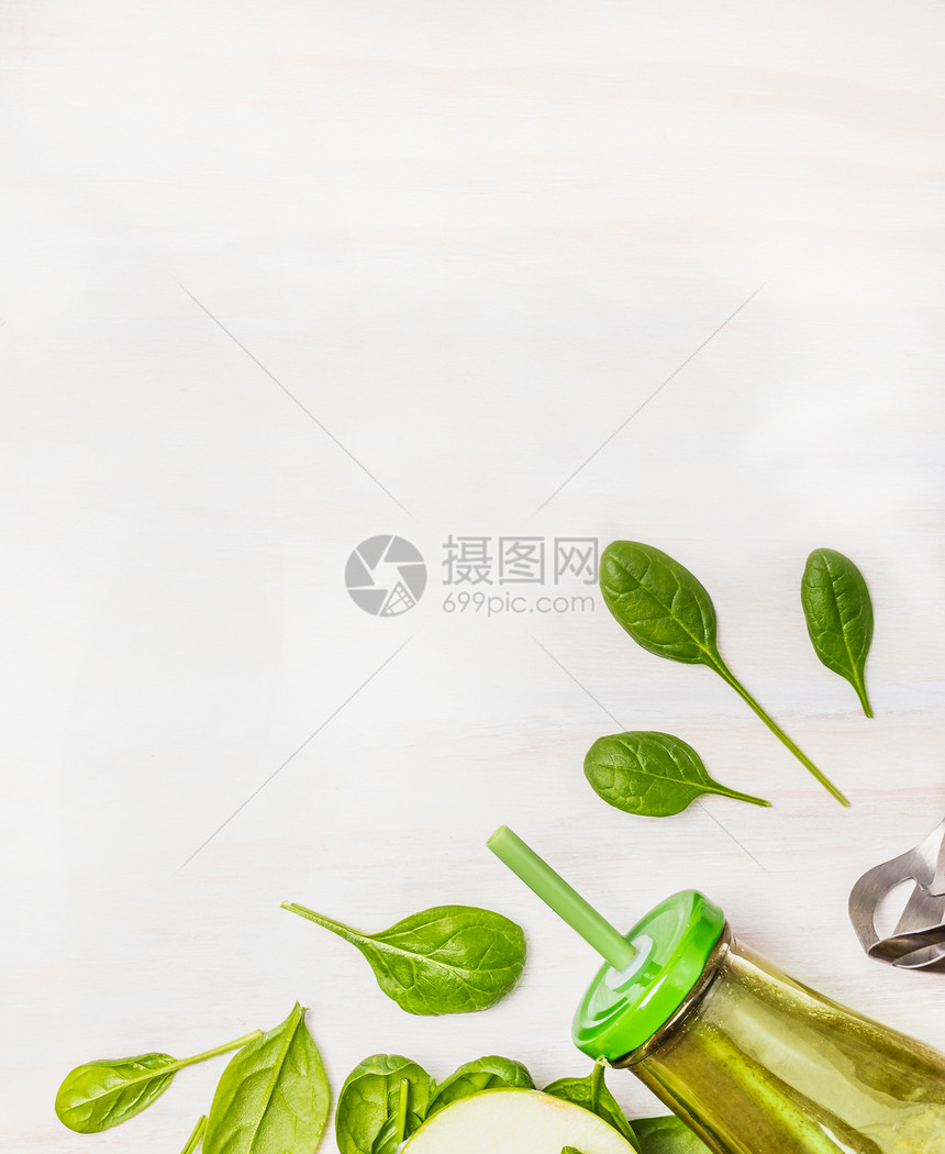 绿色冰沙璃瓶与菠菜叶白色木制背景,顶部视图,边框超级食物健康排饮食的图片