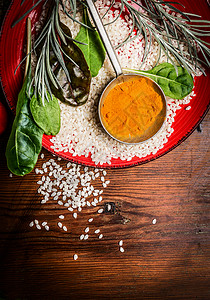 米饭咖喱粉与新鲜调味料红盘乡村木制背景图片