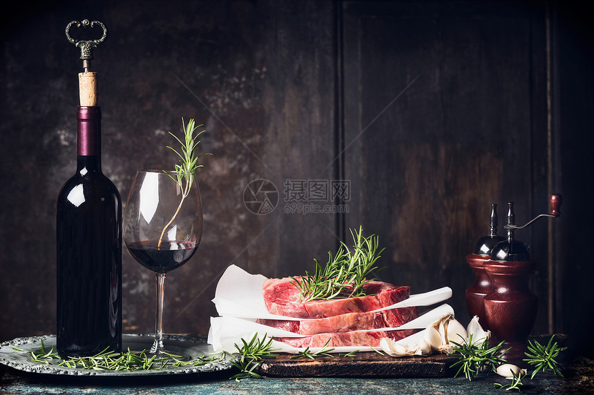 晚餐准备与生牛排,瓶子杯红酒,迷迭香盐胡椒瓶厨房桌子上的深色木制背景,侧视,文字的地方图片