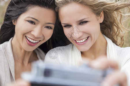 两个轻的女孩子,个亚洲华人,个金发女郎,笑着用数码相机自拍图片