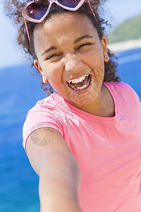厚颜无耻的自拍照片笑快乐混合种族非裔美国女女孩戴太阳镜明亮的阳光下度假蓝色热带海洋背景