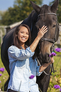 三十代快乐的美丽快乐的亚洲欧亚青妇女女孩穿着牛仔衬衫,微笑着带领她的马阳光下背景