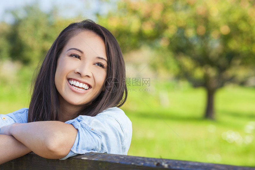 美丽快乐的亚洲欧亚青妇女女孩穿着牛仔衬衫,微笑与完美的牙齿,阳光下靠篱笆上图片