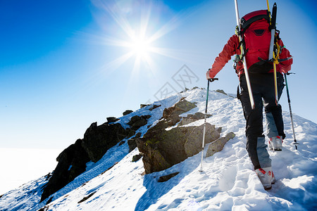 登山者沿着陡峭的雪岭行走,背包里滑雪板背景中,片戏剧的天空,着闪亮明亮的太阳冒险成就勇气决心自背景图片
