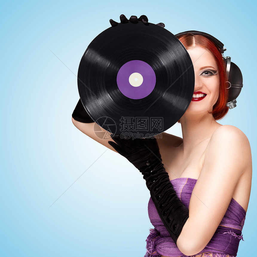 她戴着老式音乐耳机,手里着蓝色背景的紫色LP微槽乙烯基唱片图片