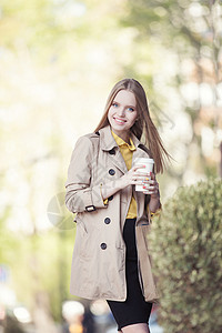 美丽的轻女人,带着次咖啡杯,喝咖啡,城市背景下微笑图片