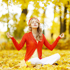 美丽的轻女子坐秋季公园的莲花瑜伽姿势图片
