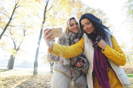 女人公园自拍秋天,美丽的轻女公园的户外用智能手机自拍图片