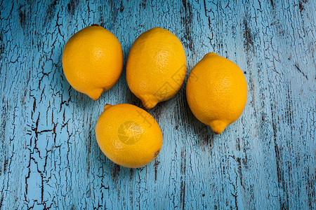 蓝色木制背景上的四个新鲜成熟的黄色柠檬图片