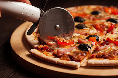 比萨饼切割机轮切火腿比萨饼与辣椒橄榄木板上的桌子高清图片