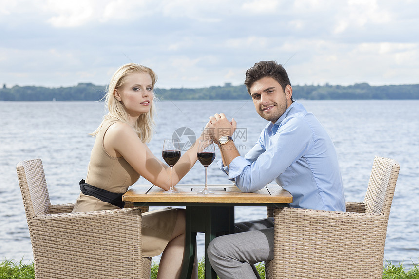 湖边户外餐厅的轻夫妇牵手的侧景肖像图片