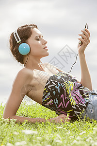 轻女子MP3播放器听音乐,用耳机,同时躺草地上抗天空图片