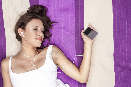 放松的女人听音乐mp3播放器用耳机,同时躺野餐毯上图片