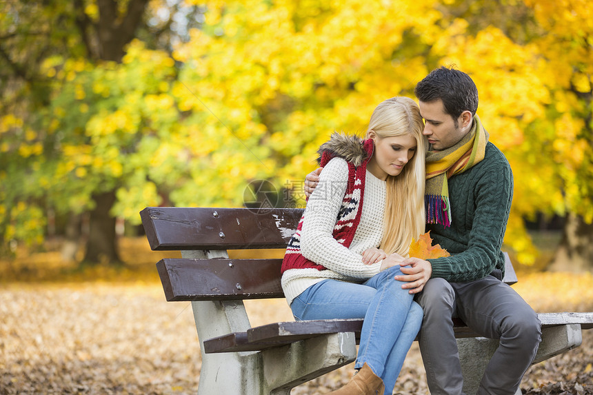 秋天,热情的轻人公园的长凳上拥抱害羞的女人图片