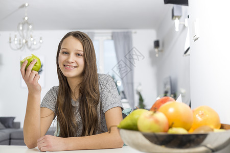 微笑的女孩坐家里的桌子上着苹果的肖像图片