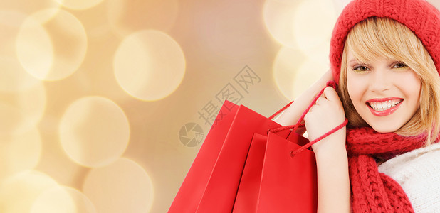 幸福,寒假,诞节人们的微笑的轻女人戴着帽子围巾,米灯光背景下红色的购物袋图片