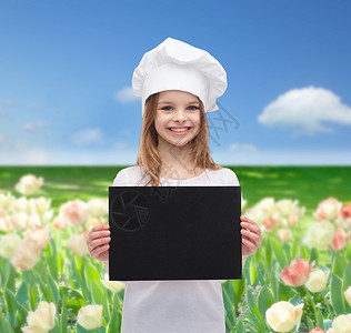 烹饪,童,广告人的微笑的小厨师女孩,厨师包师用空白的黑纸蓝天田野的花朵背景图片