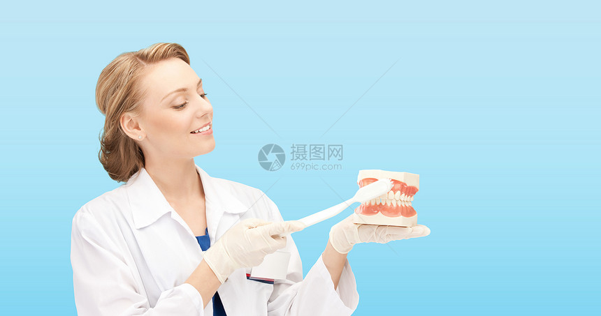 医学,口腔医学,人与卫生微笑的女医生用牙刷颌骨模型教如何蓝色背景下刷牙图片