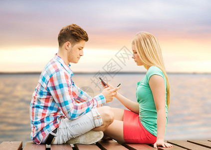 夏天的海滩,假期,技术,成瘾友谊的夫妇与智能手机坐长凳上日落海边图片