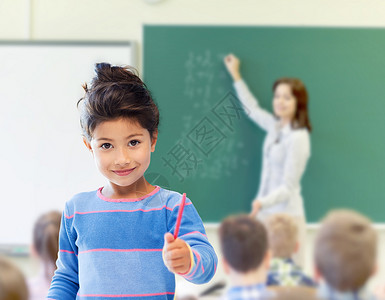 教育,小学儿童快乐的小学生女孩用钢笔教室老师写绿色黑板的背景图片