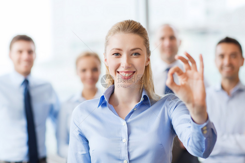 商业,人,手势队合作的微笑的女商人与办公室里的群商人表现出良好的迹象图片