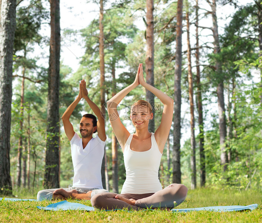 运动,健身,瑜伽人的微笑的夫妇冥想坐垫子上,举手绿色的树林背景图片