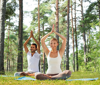 运动,健身,瑜伽人的微笑的夫妇冥想坐垫子上,举手绿色的树林背景图片