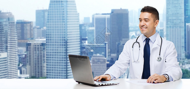 医学,专业,技术人的微笑的男医生坐桌子上,笔记本电脑听诊器城市背景图片