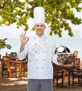 陈腔滥调烹饪,职业,手势人的快乐的男厨师着克洛奇,并海滩上的餐厅休息室OK标志背景