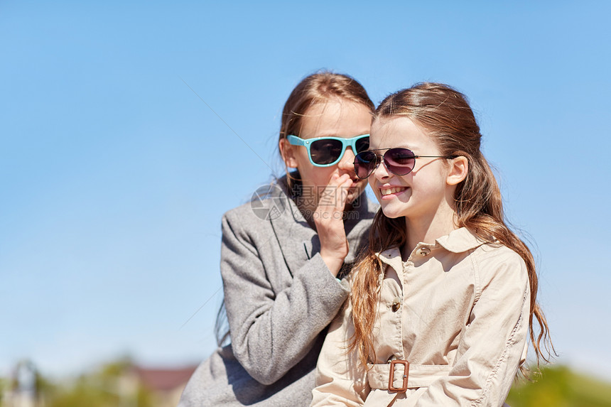 人孩子友谊的戴太阳镜的快乐小女孩向朋友耳语她的秘密户外闲聊图片