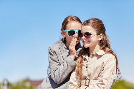 人孩子友谊的戴太阳镜的快乐小女孩向朋友耳语她的秘密户外闲聊图片