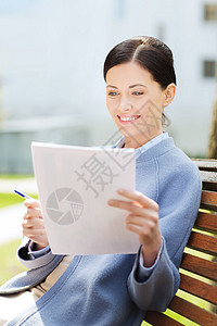 商业,文书工作人的轻的微笑女商人阅读文件坐城市长凳上图片