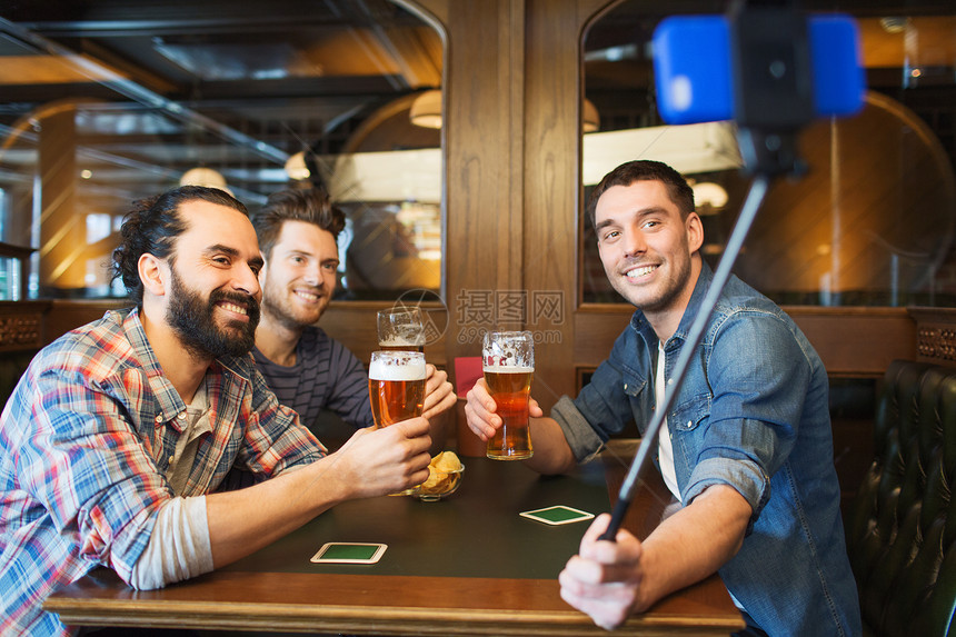 人男人休闲友谊技术快乐的男朋友酒吧酒吧喝啤酒,用智能手机自拍棒拍照图片
